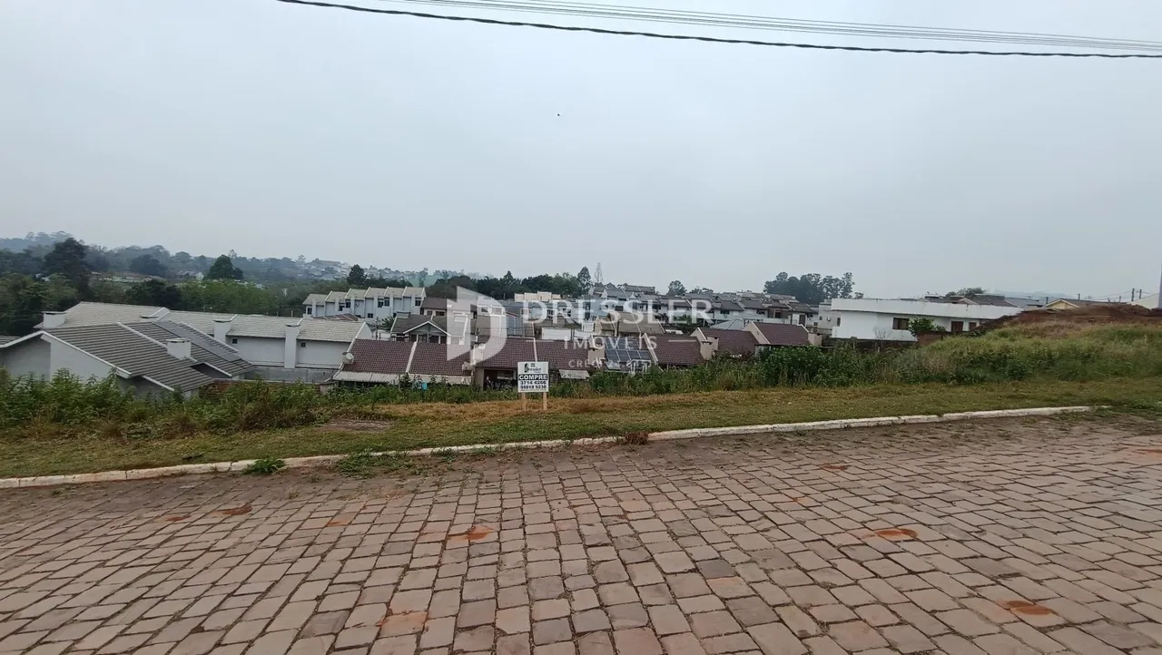 Vista externa de uma propriedade com casas ao fundo e um pátio pavimentado na frente.