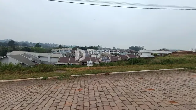 Vista externa de uma propriedade com casas ao fundo e um pátio pavimentado na frente.