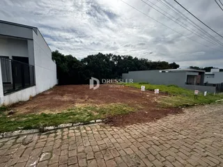 Vista externa de uma propriedade com um terreno gramado e uma área pavimentada na frente.