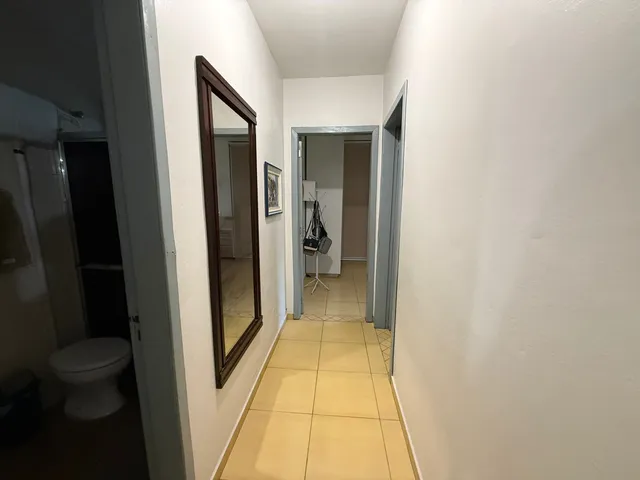 Uma foto de um corredor interno com paredes brancas e piso de cerâmica.