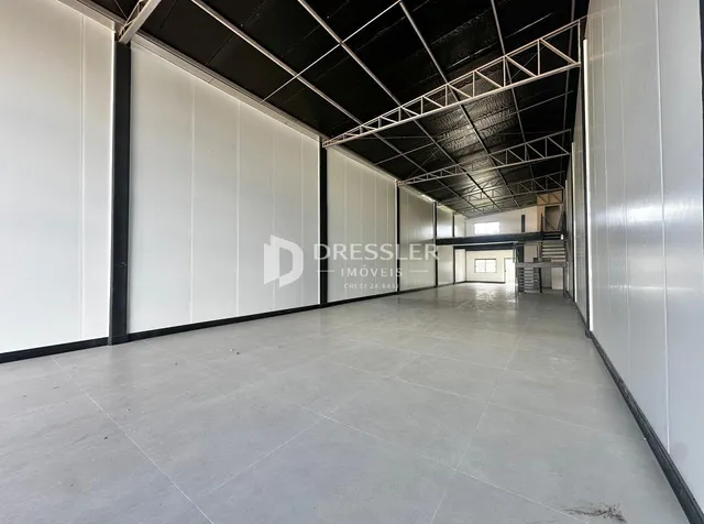 Espaço interno amplo com paredes brancas e estrutura de teto industrial.