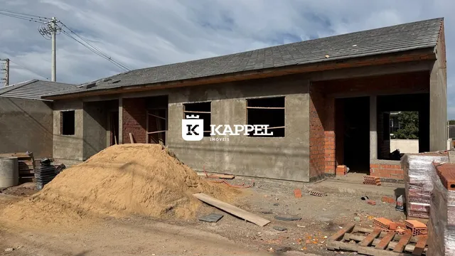 Fachada de uma construção em Lajeado, Brasil, mostrando paredes de concreto e terra no primeiro plano.