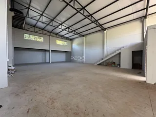 Imagem de um espaço amplo com estrutura de telhado metálico e piso de concreto.