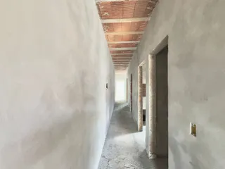 Corredor longo e estreito com paredes brancas e teto exposto.