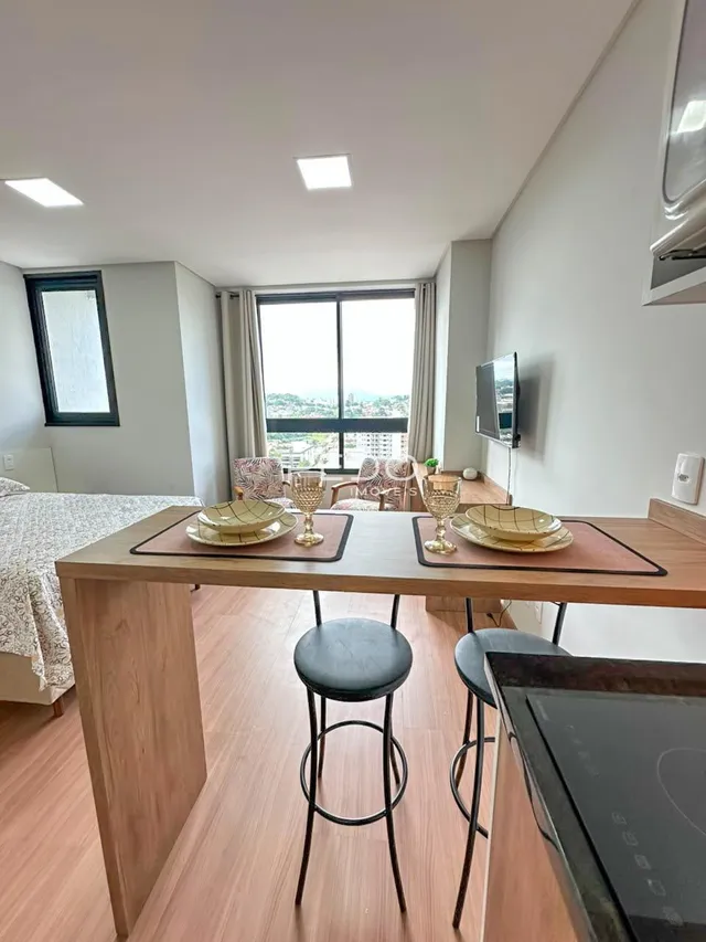 Vista de uma sala de jantar com piso de madeira clara e grande janela.