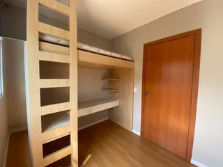 Quarto com estrutura de cama alta de madeira e porta de madeira em um ambiente claro.