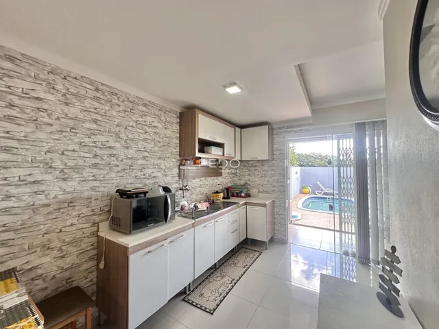 Cozinha moderna com armários brancos e piso de cerâmica com vista para a piscina externa.